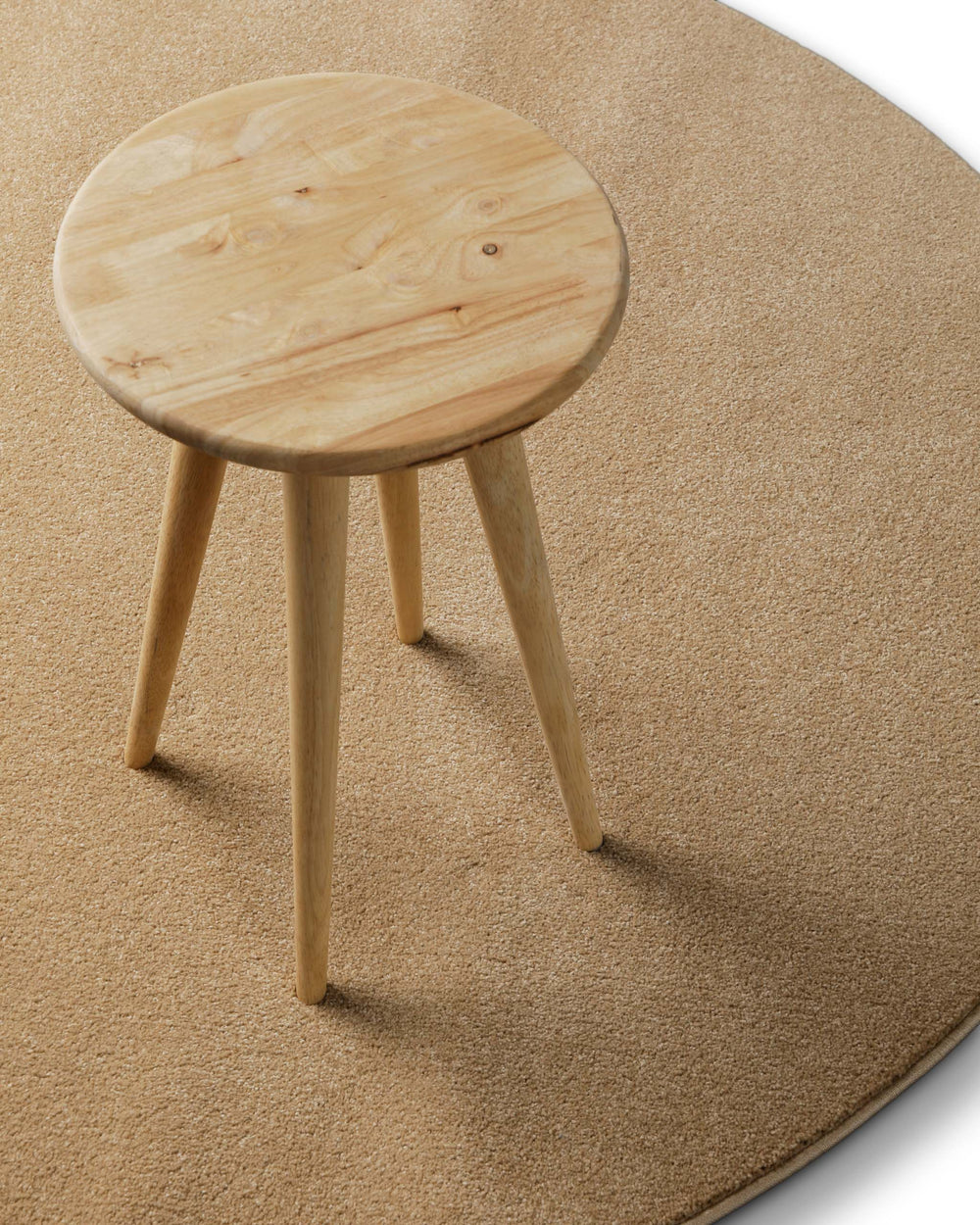Freja Teppich rund in sandfarben im Raum inszeniert, kombiniert mit Hocker für ein warmes Gesamtbild
