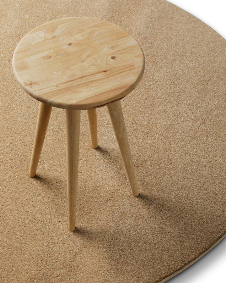 Freja Teppich rund in sandfarben im Raum inszeniert, kombiniert mit Hocker für ein warmes Gesamtbild