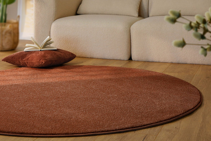 Kurzflor Teppich Vegas Rot rund im Wohnzimmer auf Holzboden, Fläche vor Sofa mit gleichmäßiger Oberfläche
