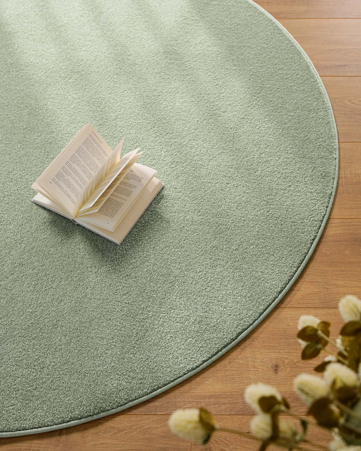 Kurzflor Teppich Vegas Hellgrün rund Nahaufnahme mit Buch auf der Fläche, gleichmäßiger Kurzflor erkennbar