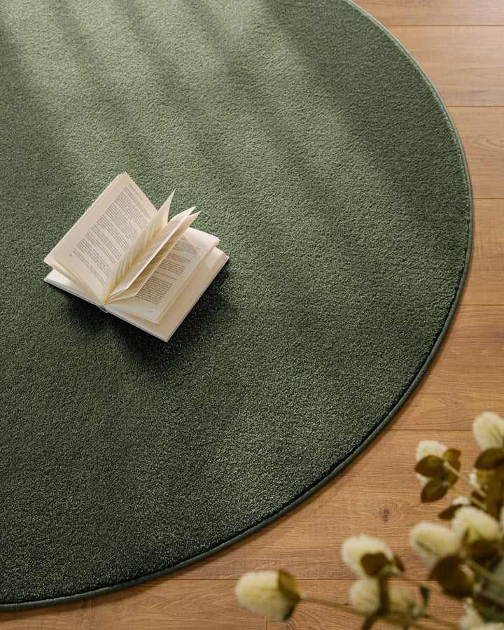 Kurzflor Teppich Vegas Grün rund Nahaufnahme im Wohnraum mit Buch auf der Fläche, gleichmäßiger Kurzflor sichtbar