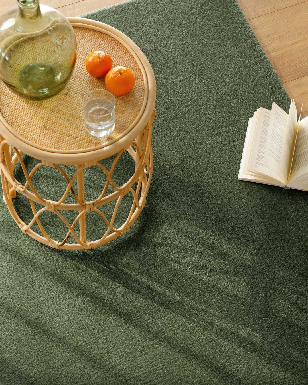 Kurzflor Teppich Vegas Grün Nahaufnahme im Wohnraum, Beistelltisch mit Glas und Buch auf der Teppichfläche