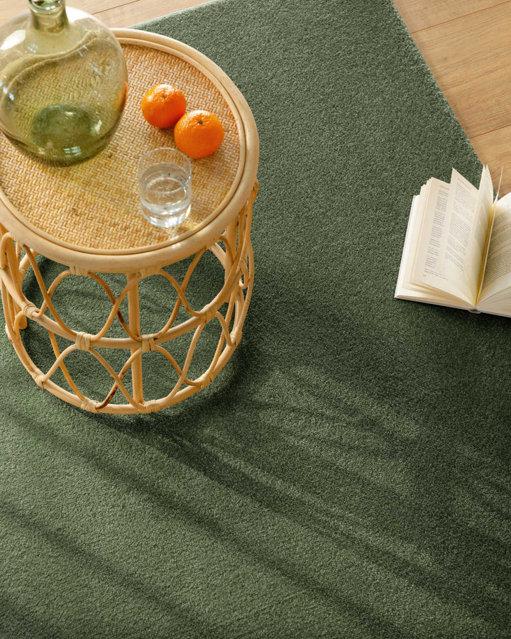 Kurzflor Teppich Vegas Grün Nahaufnahme im Wohnraum, Beistelltisch mit Glas und Buch auf der Teppichfläche