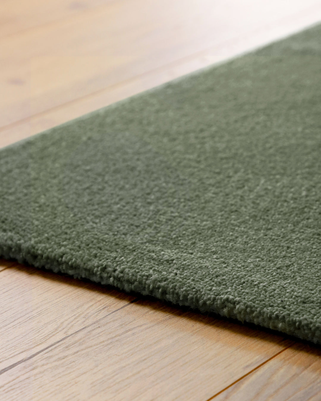 Kurzflor Teppich Vegas Grün Detail der Teppichkante auf Holzboden, flacher Abschluss und feine Struktur sichtbar