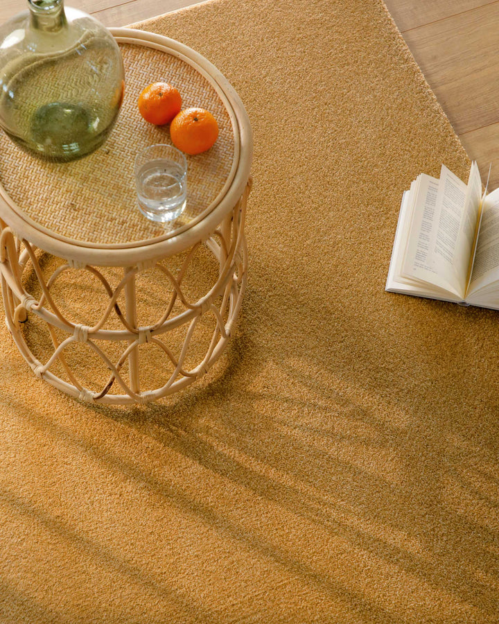 Kurzflor Teppich Vegas Ocker Gelb Detail mit Tisch und Deko, Licht fällt schräg über die Oberfläche